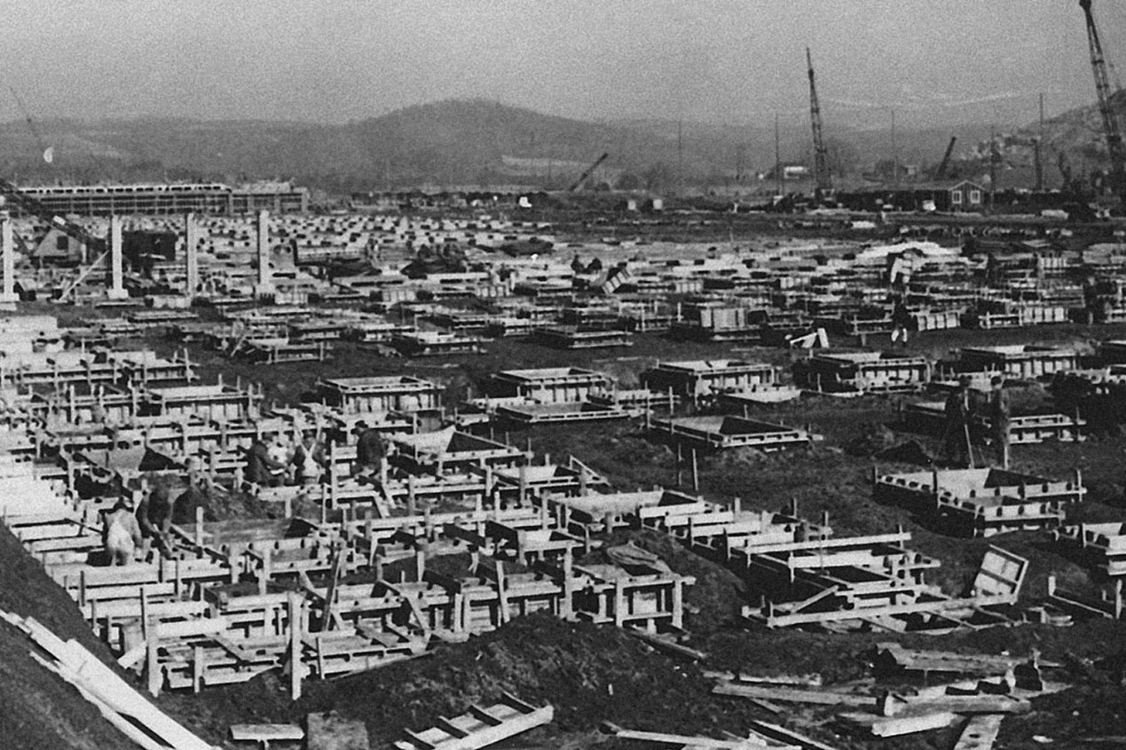 Κατασκευή θεμελίων κτιρίου του K-25: εκτεταμένο εργοτάξιο με θεμέλια από σκυρόδεμα, γερανούς και λόφους στο βάθος.